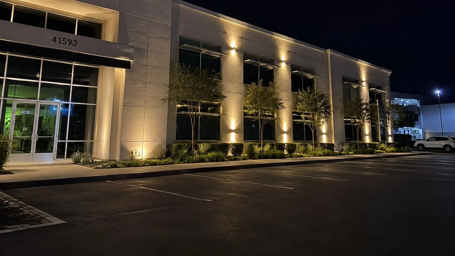 Class-A office building at dusk with wall-pack up and downlighting along the facade and tree uplighting in the foreground